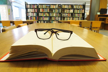 A glasses on the open old book in library. Selective focus with blurred background.