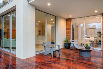 Wet wooden deck with furniture and open doors leading to inside.