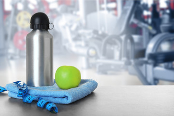 Bottle, measuring tape and towel on table against blurred gym interior background