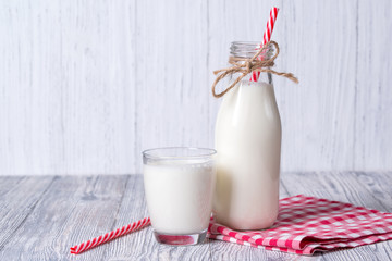 Bottle and glass of milk with red straw, white wooden background