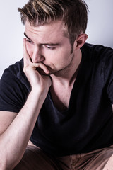 Fototapeta premium smutny mężczyzna w czarnej koszulce z ręką na głowie siedzi na co