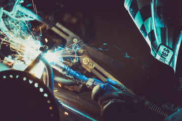Man welding steel pipe on a work table in an Industrial workshop, producing blue and green smoke, hot sparks