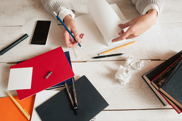 Workplace of hardly studying woman flat lay. Top view on female hand writing in notebook on messy desk with supplies and paper wads. Stress, idea crisis, failure, lack of inspiration concept © golubovy
