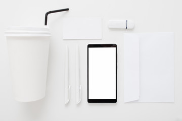 Smartphone with blank screen and office stuff flat lay. Top view on set of white supplies with black mobile phone. Business, stationery, modern life, contrast, brendbook, commercial concept