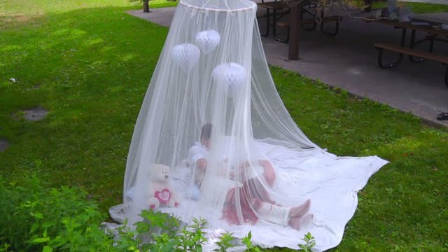 Tender couple resting behind white veil on green grass. Love couple relax on green grass behind transparent fabric. Romantic couple relaxing outdoor. Two people laying under wedding canopy