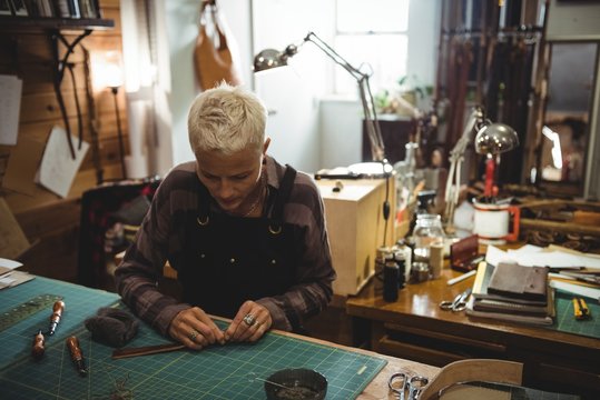 Attentive craftswoman cutting a piece of leather