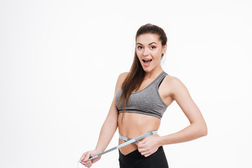 Happy surprised sports woman holding tape measure around her waist