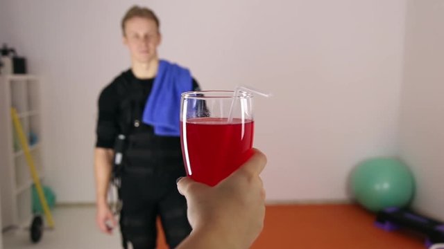 The girl's hand holds out a glass of juice athlete, standing at a distance