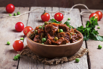 Ragout with beef, carrots, green peas and tomatoes, old wooden b