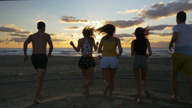 Group of young friends running into the water from the beach at sunset