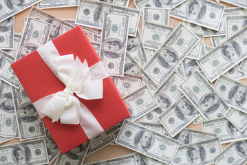 Red gift box with white ribbons on pile of dollars banknotes fla