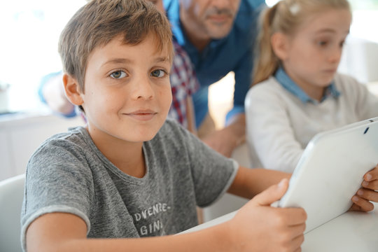 Portrait of schoolboy in classroom learning with digital tablet