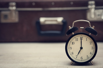 retro style image of alarm clock showing seven with vintage suitcase on the background. closeup.