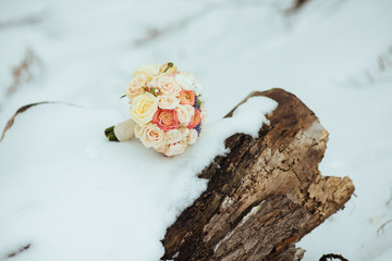 beautiful wedding bouquet with ribbons lies in the woods near a tree in the winter