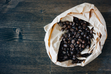 Coffee beans - roasted seeds of coffee in paper bag over the wood board