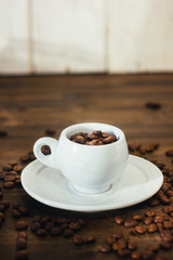 Coffee beans on white coffee cup over the wooden table.