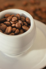 Coffee beans on white coffee cup over the wooden table.