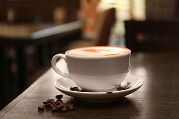Cup with hot tasty coffee on wooden table in cafe, close up view