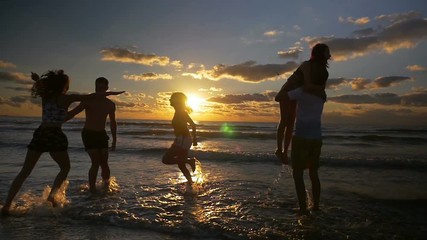 Group of people jumping dancing and having fun in the water on beach at sunset in slow motion