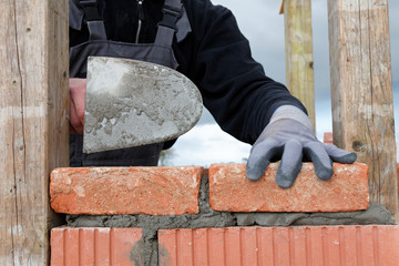 Close up of bricklayer mason hands installing brick on wall