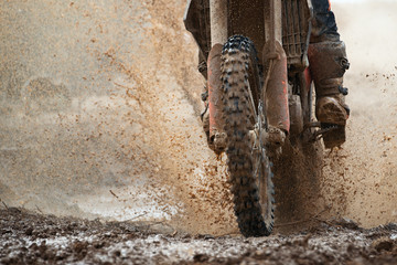 Motocross driver splashing mud on wet and muddy terrain
