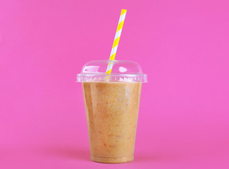 Tasty peach milkshake in plastic cup on pink background