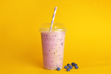 Delicious berry milkshake in plastic cup on yellow background