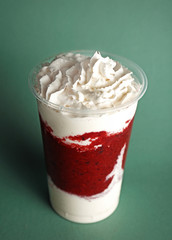 Delicious strawberry dessert with cream in plastic cup on green background