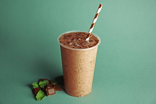 Tasty chocolate milkshake in plastic cup on green background