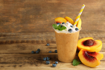 Tasty peach milkshake with cream and blueberry in plastic cup on wooden background