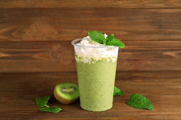 Delicious kiwi milkshake in plastic cup on wooden background