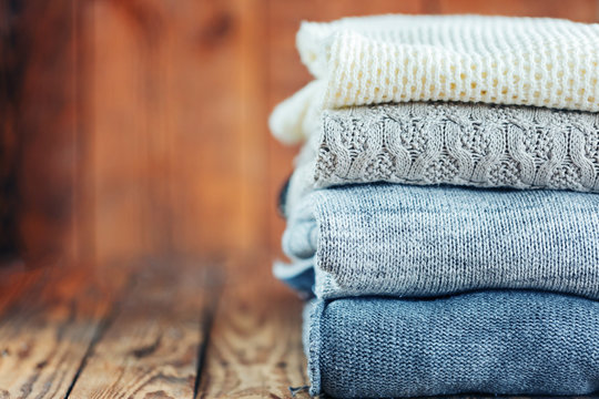 Stack of knitted winter clothes on wooden background, sweaters, space for text. Toned image.