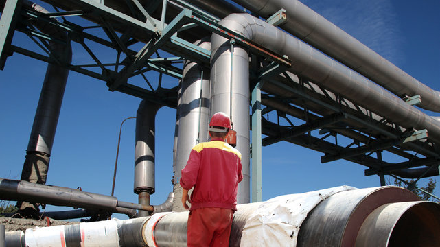 Oil and Gas Pipelines Construction / Worker in front of industrial pipelines on pipe-bridge against blue sky