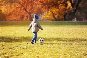Cute little boy playing football on soccer pitch