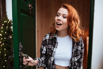 Fototapeta na wymiar Pretty young woman with red hair open the door