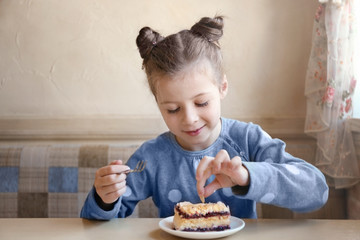 Cute little girl eating tasty cake in kitchen