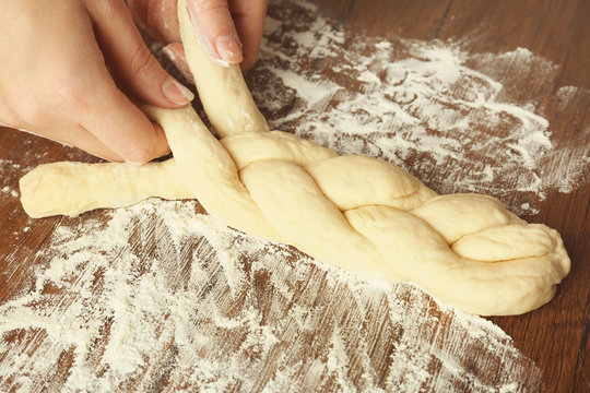 Woman preparing tasty braided bun on kitchen table, close up - Powered by Adobe