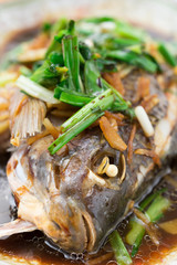 fresh steamed whole fish covered with herbs onions and sauce close up