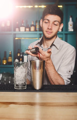 Young handsome barman pouring cocktail drink into glass
