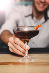 Young Barman offers alcohol cocktail in night club bar