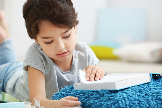 Cute little boy lying with book on blurred background