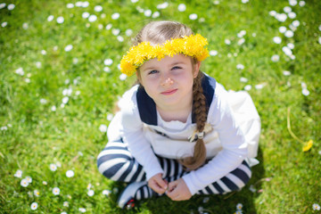Top view of a cute girl with dandelion wreath on spring meadow