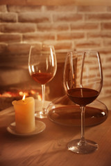 Decanter, glasses with red wine and candle on wooden table against fireplace