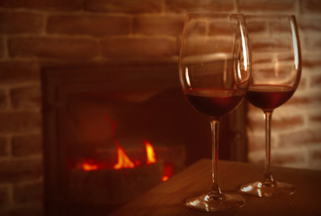 Two glasses with red wine on wooden table against fireplace