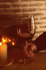Male hand and glass of red wine on wooden table against fireplace