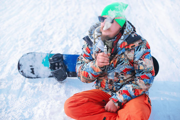 snowboarder resting on ski slope, vaping Electronic Cigarette ,winter sports concept. Close-up
