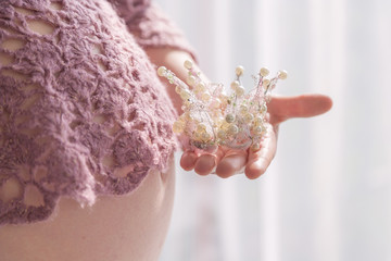 Close up of a belly and mothers hand holding a little crown