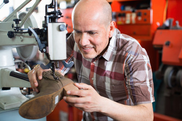 Mature workman sewing leather boots on stitch lathe