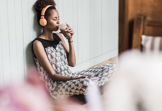 Young woman sitting on floor drinking from glass and listening to music