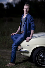 Obraz premium Mann in 50er 60er Jahre retro Fashion sitzt auf der Motorhaube eines Ildtimers